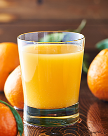 A glass of orange juice with whole oranges surrounding it. 