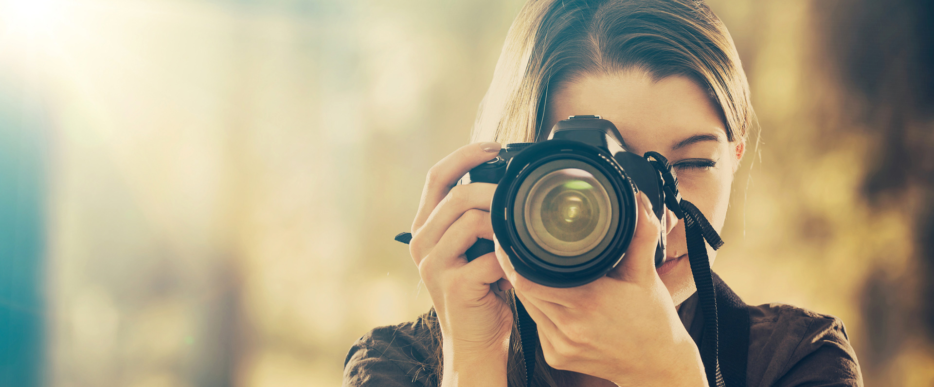 A female in a brown shirt looking through the viewfinder of an SLR camera. Links to the Image Gallery. 