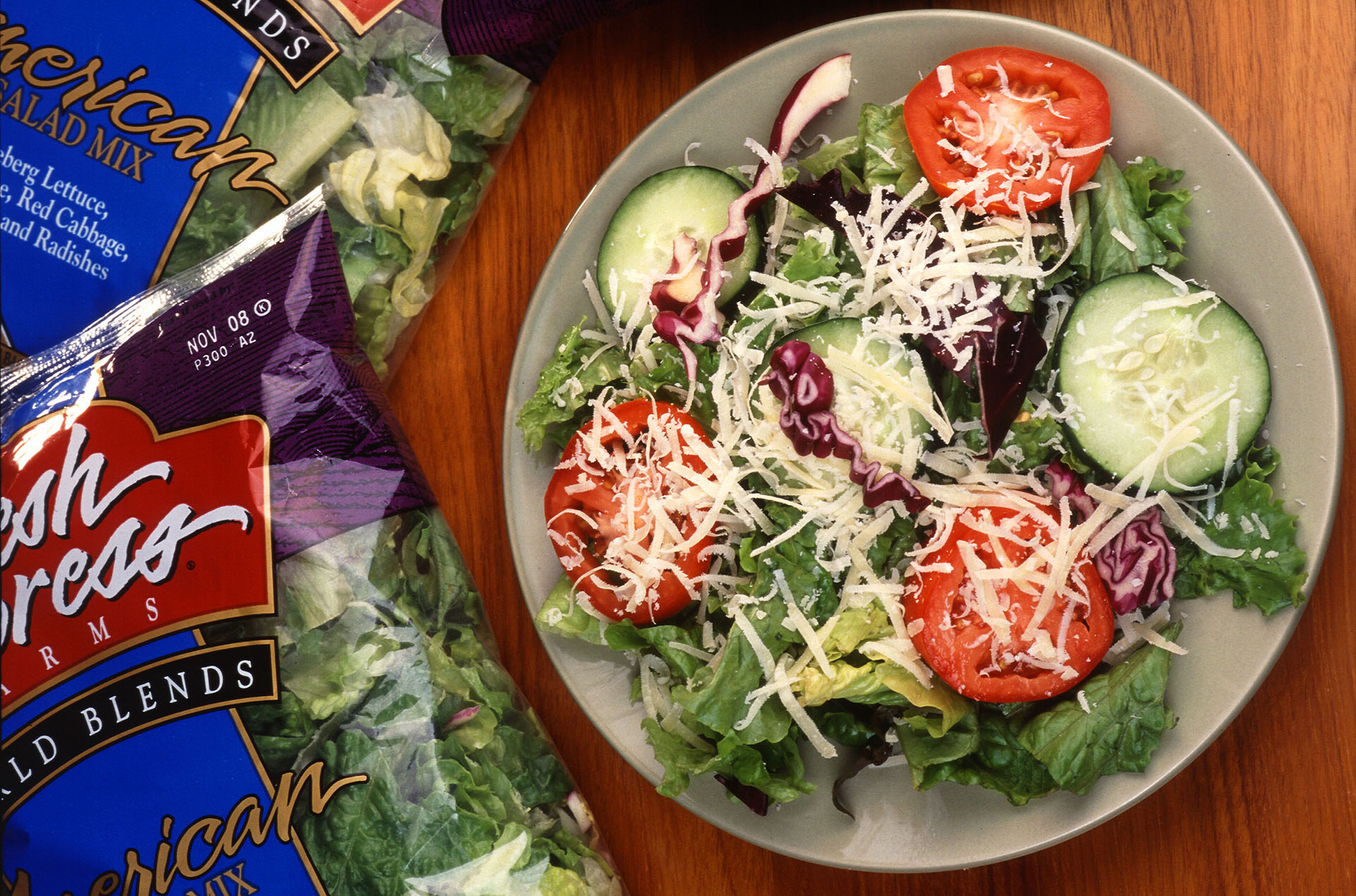 A plate of salad greens, sliced tomatoes, cucumbers and shredded cheese