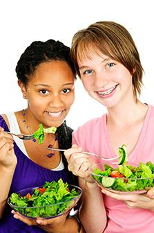 Two girls each holding a fork and bowl of salad greens. 