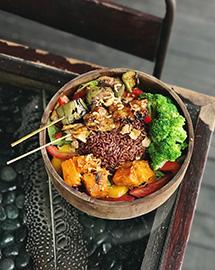 A bowl of broccoli, butternut squash chunks, tomatoes slices, seeds, peppers and other vegetables.    