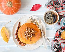 Pumpkin pancakes with pecan nuts, honey and cup of coffee on white table. 