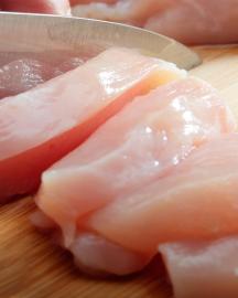 A knife slicing raw chicken