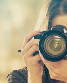 A female in a brown shirt looking through the viewfinder of an SLR camera. Links to the Image Gallery. 