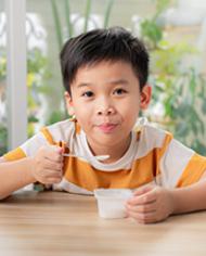 A young Asian boy eating yogurt
