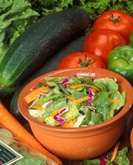 A bowl of salad--fresh tomatoes, cucumbers and green peppers surround the bowl 