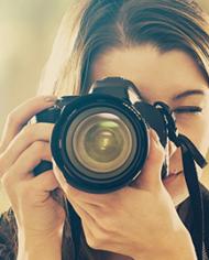 A female photographer looking through the lens of a DSLR camera. 