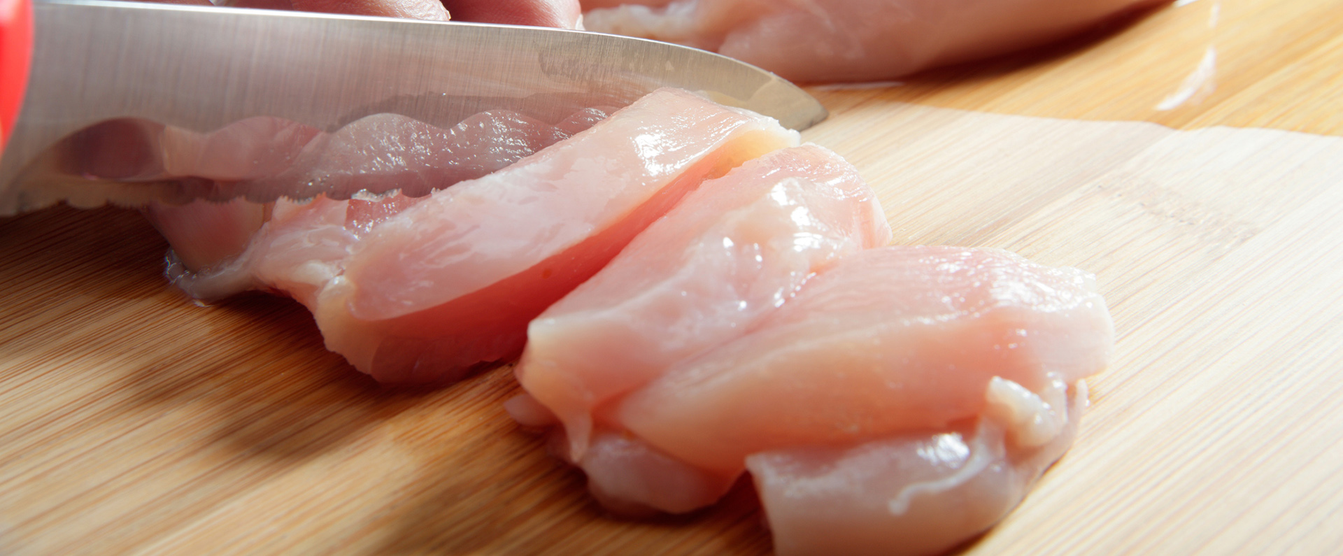 A knife slicing raw chicken