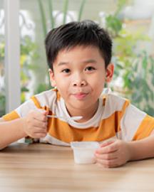 A young Asian boy eating yogurt