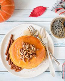Pumpkin pancakes with pecan nuts, honey and cup of coffee on white table. 